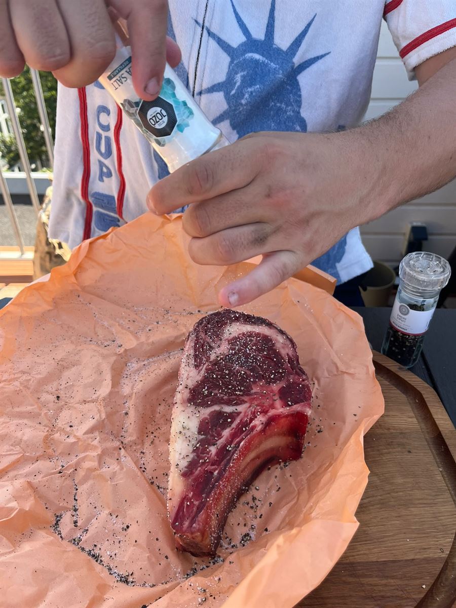Mani che condiscono una costata cruda con sale e pepe sulla carta del macellaio